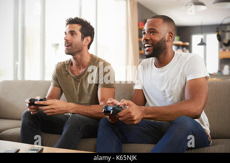 Two Male Friends Sitting On Sofa In Lounge Playing Video Game Stock Photo