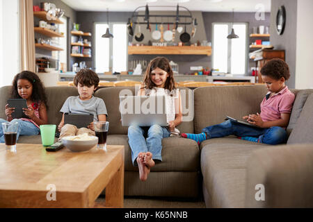 Group Of Children Sitting On Sofa Using Digital Devices Stock Photo
