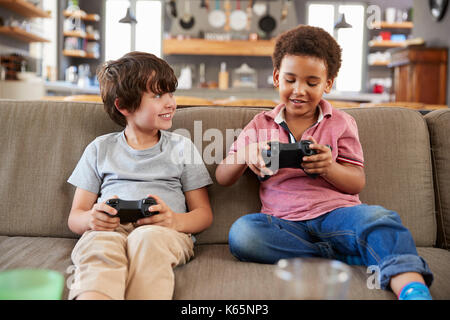 Two Boys Sitting On Sofa In Lounge Playing Video Game Together Stock Photo