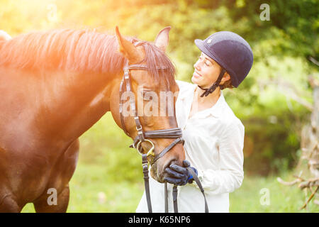 Young beautiful rider woman in helmet holding bay horse by bridle Stock Photo
