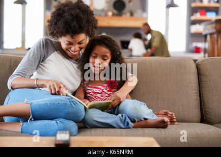 Mother And Daughter Sit On Sofa In Lounge Reading Book Together Stock Photo