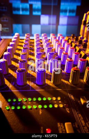 Close-up of audio mixing desk with background computer screen. Selective focus on foreground controls Stock Photo