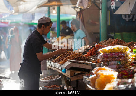 Kyrgyz seller arranging dried fruit and spices at food market stall in the city Osh along the Silk Road in Kyrgyzstan Stock Photo