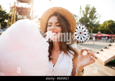 Close up portrait of a smiling young girl eating cotton candy at amusement park Stock Photo