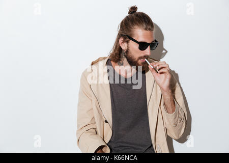 Image of a hipster man looking aside isolated over wall background holding cigarette. Stock Photo