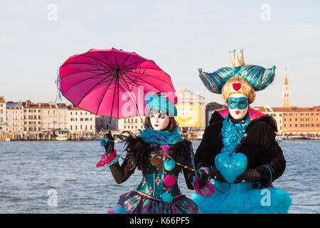 Venice Carnival 2017, Veneto, Italy, Colorful  couple in costumes and masksposing in front of the lagoon with the Castello city skyline  behind them Stock Photo
