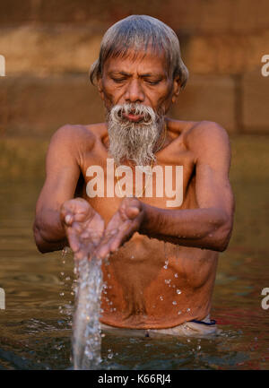 VARANASI, INDIA - CIRCA NOVEMBER 2016: Man worshiping in the Ganges river in Varanasi. Varanasi is the spiritual capital of India, the holiest of the  Stock Photo