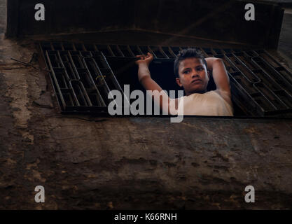 VARANASI, INDIA - CIRCA NOVEMBER 2016: Portrait of a young boy looking through a windown in Varanasi. Stock Photo