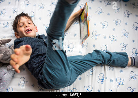 Playful Mixed Race boy laying on bed holding digital tablet Stock Photo