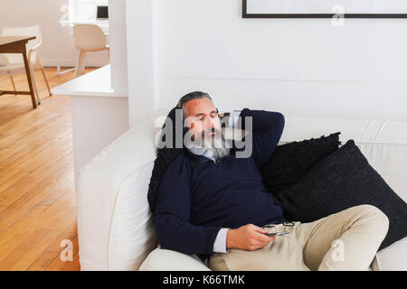 Caucasian man on sofa listening to cell phone with headphones Stock Photo