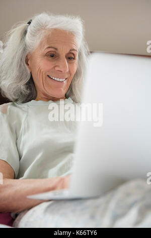 Older woman laying in the bed using laptop Stock Photo