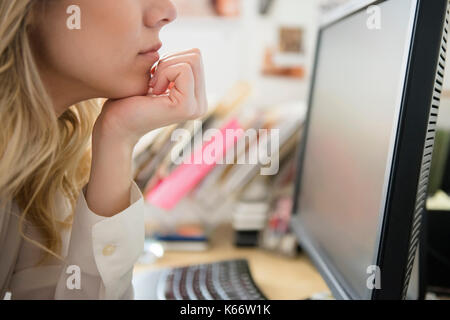 Caucasian woman with hand on chin reading computer Stock Photo