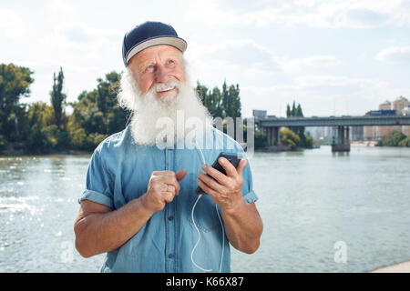 Bearded stylish mature man in headphones is listening to music using a smartphone Stock Photo