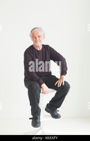 Older Caucasian man sitting on stool Stock Photo