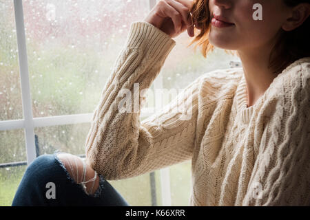 Portrait of pensive Caucasian woman near rainy window Stock Photo