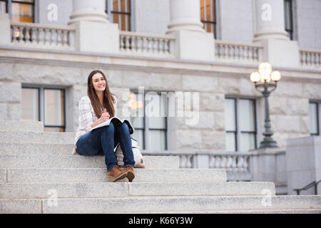 Smiling Caucasian woman sitting on staircase holding notebook Stock Photo