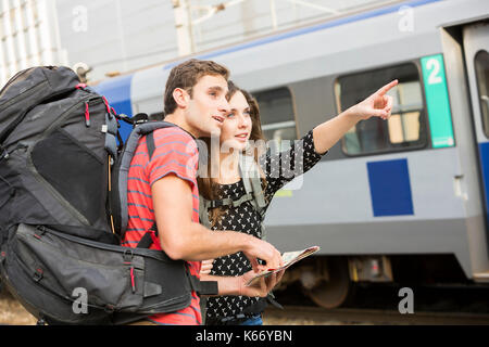 Caucasian couple reading map near train and pointing Stock Photo