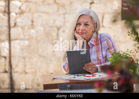 Pensive older Caucasian woman using digital tablet Stock Photo