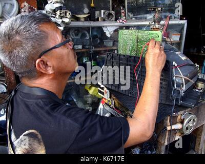 ANTIPOLO CITY, PHILIPPINES - SEPTEMBER 7, 2017: An electrician repairs an old television set at his repair shop. Stock Photo