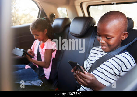 Boy and girl in a car using tablet and smartphone on a trip Stock Photo