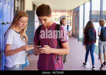 Two friends talking and using phones in school corridor Stock Photo