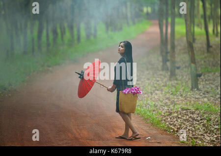 Woman walking along footpath carrying a parasol, Thailand Stock Photo