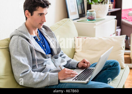 Young handsome man browsing the internet on laptop at home Stock Photo