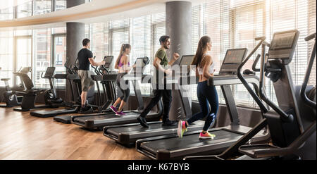 Group of four people running on treadmills in fitness gym Stock Photo