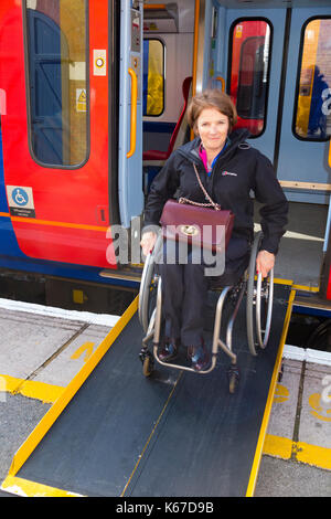 Wheel chair user / person in a wheelchair departing / leaving / alighting from a train carriage onto a platform using a ramp provided at the station. Stock Photo