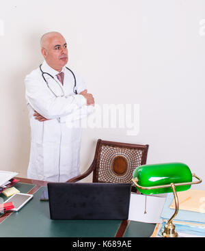 Aback doctor in his studio. Use new technologies. The office has an antique desk and a green lamp shade of green. Stock Photo