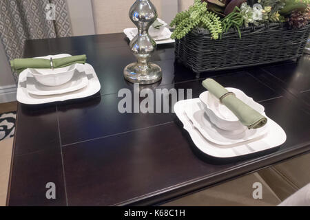 Place settings around a brown dining room table with bowls and green napkins laid out. Stock Photo