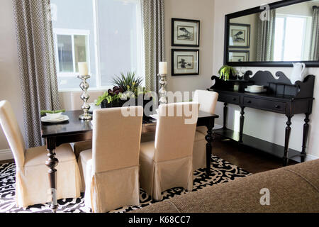 A dining room table with white cloth chairs and a freiburg stand in the corner. Stock Photo