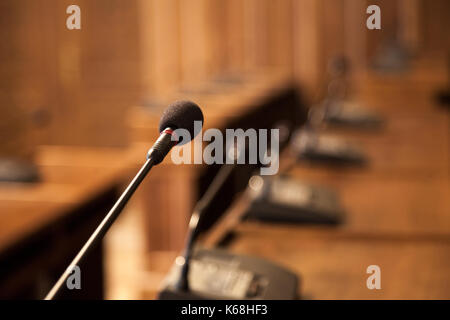 Close up on a microphone in a conference room of a municipal assembly. Other similar microphones can be seen in the background, in a vintage room  Pic Stock Photo