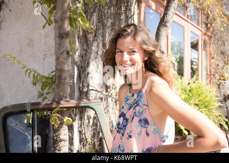Portrait of a young woman with long  brown hair standing outside vintage shop in sunny quaint street. Stock Photo