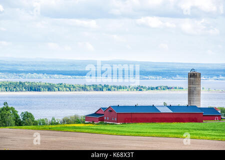 Aerial cityscape landscape view of farmland in Ile D'Orleans, Quebec, Canada, plowed field, furrows, farm and grain storage silo barn, shed or by Sain Stock Photo
