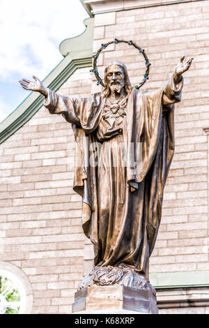 Ile D'Orleans, Canada - June 1, 2017: Saint-Jean church parish with stone architecture and Jesus Christ statue with outstretched open arms and illumin Stock Photo