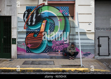 SAN TELMO, BUENOS AIRES, ARGENTINA - SEPTEMBER 2017 - Unidentified man sitting in the street and behind a graffiti Stock Photo