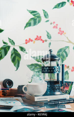 Brewing coffee in French press with rising steam and books about photography. Creative workplace. Professional barista at work. Light cafe interior. Stock Photo