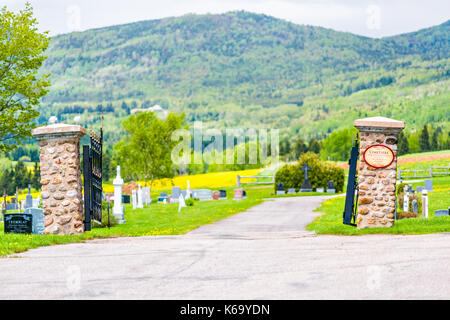 Les Eboulements, Canada - June 2, 2017: Presbytere Des Eboulements cemetery in Charlevoix region of Quebec with open gate, tombstone, graves, mountain Stock Photo