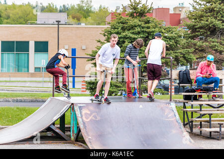 Saguenay, Canada - June 3, 2017: Downtown city summer park in Quebec with young teenagers boys skating, performing tailwhip tricks, stunts on scooter  Stock Photo