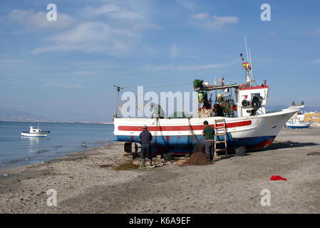 Fishermen mending their nets on a fishing boat docked on the beach at San Miguel, San Miguel de Cabo de Gata, Almeria province, Spain Stock Photo