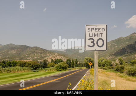 What looks to be a straight road has a sharp curve sign after the pedestrian crossing sign in this 30 mph speed limit area. Stock Photo
