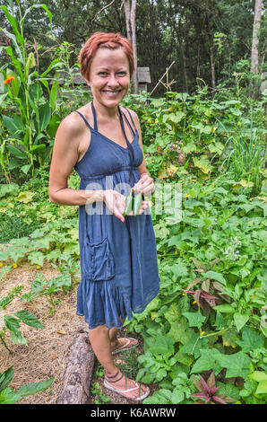 Young woman with orange hair standing in her garden with two fresh-picked jalapeno chili peppers Stock Photo