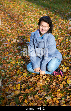 happy young teen girl in autumn scenery throwing leaves Stock Photo