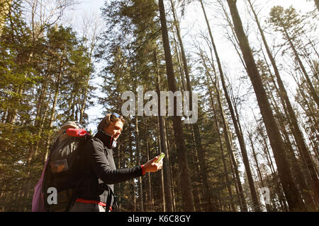 Disoriented hiker checking her phone for GPS coordinates, being lost in the woods, looking for the right direction. Adventure, active lifestyle, mobil Stock Photo