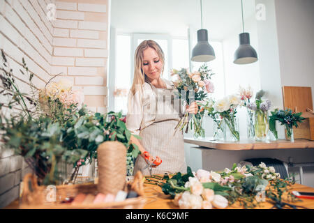 Florist workplace: woman arranging a bouquet with roses, matthiolas, ranunculus flowers and gypsophila paniculata twigs. Stock Photo