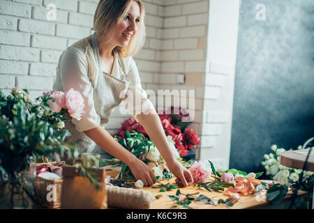 Florist workplace: woman arranging a bouquet with roses, matthiolas, ranunculus flowers and gypsophila paniculata twigs.