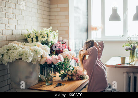 Happy beautiful young woman florist in glasses sitting in flower shop Stock Photo