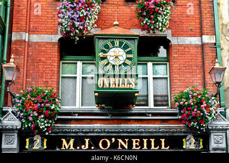 Large green clock, lamps, pub sign, flowers on the wall outside M.J. O'Neill's bar. Traditional Irish pub. Dublin. Republic of  Ireland, Europe, EU. Stock Photo