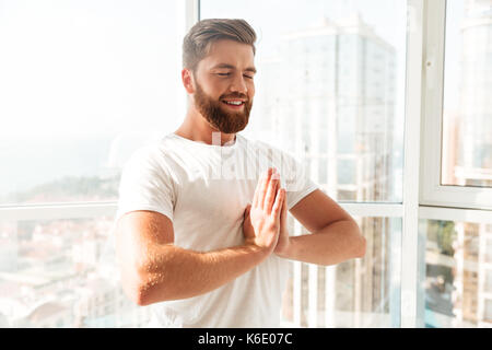 Side view of smiling bearded man meditation with closed eyes over window background at home Stock Photo